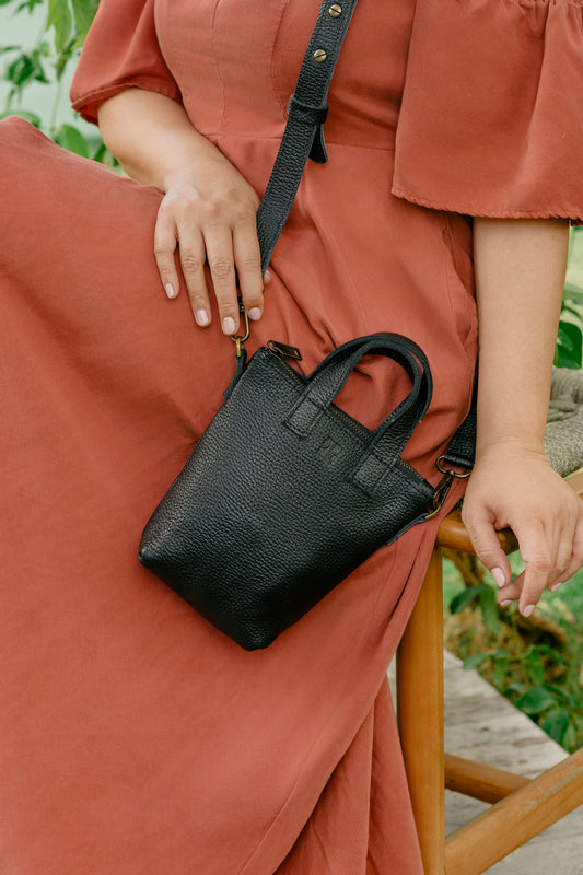 Person wearing a rust-colored dress holding a black handbag outdoors.