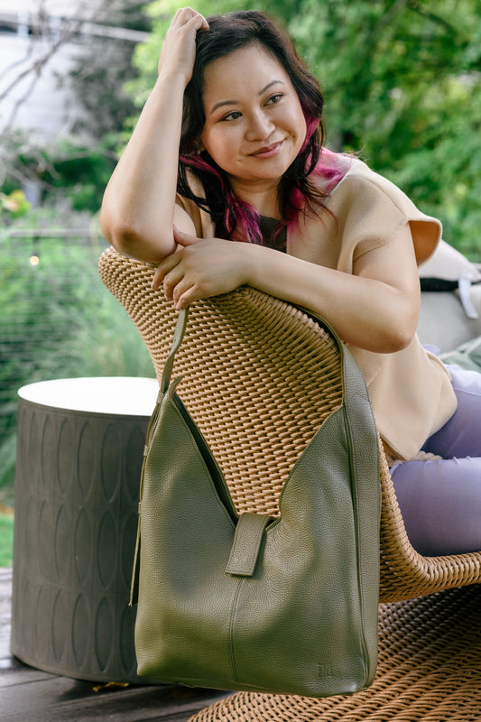 Woman holding a green leather handbag with a woven pattern, sitting outdoors.