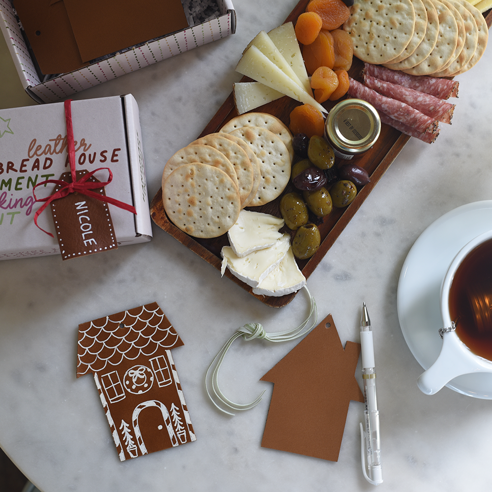 Gingerbread house ornament kit with a charcuterie board, tea, and decorative items on a marble surface.