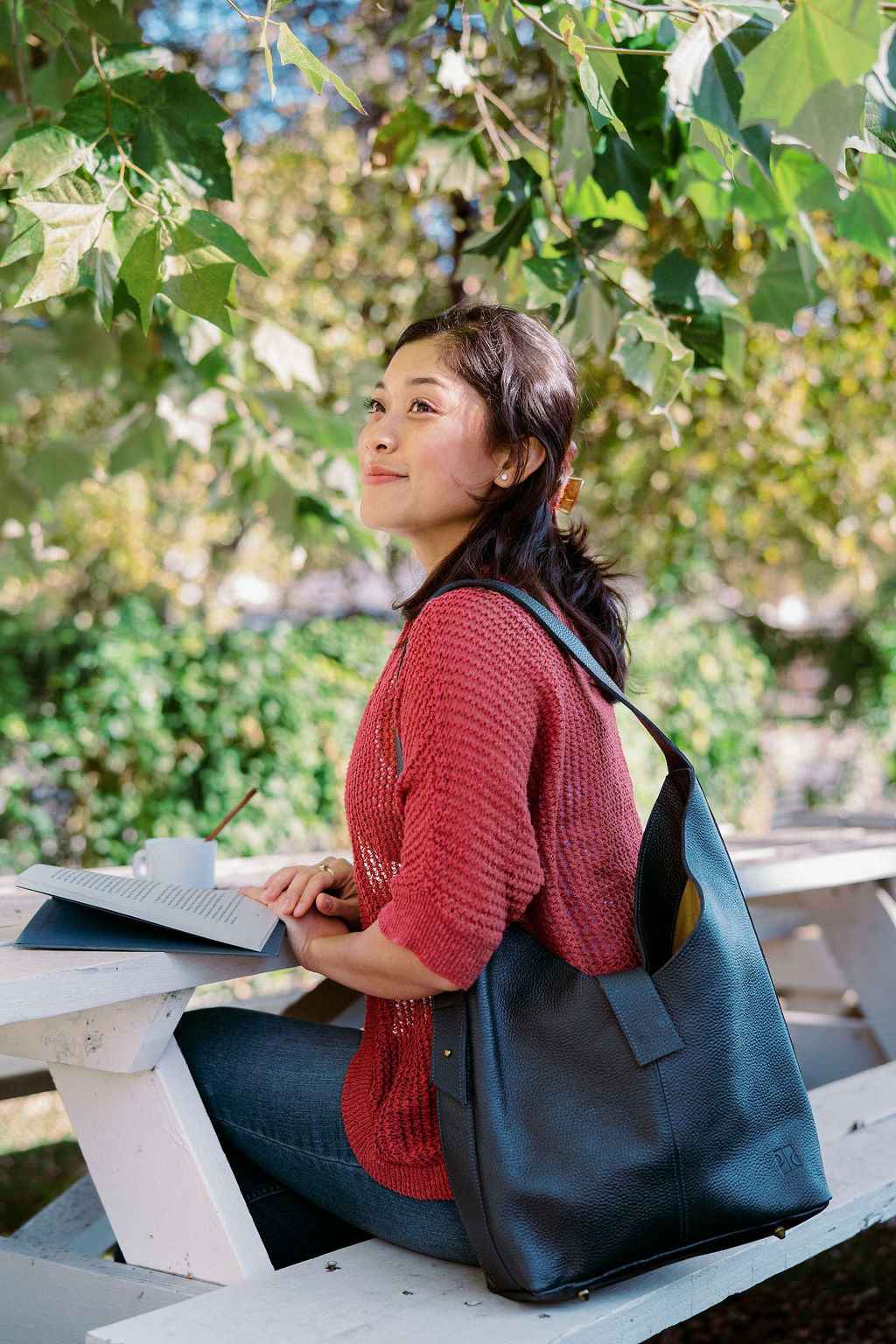 Woman sitting outdoors with a blue leather bag, surrounded by greenery