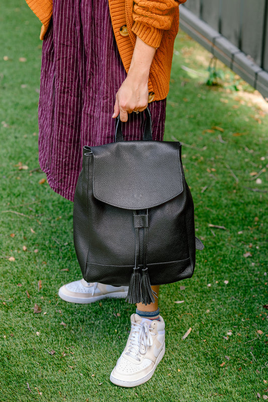 Person holding a black backpack on grass