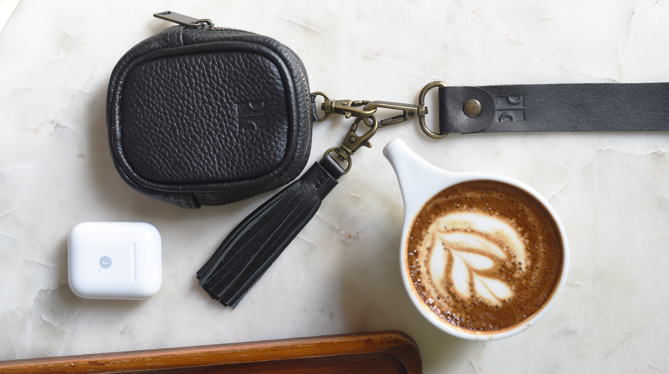 Black leather keychain case with tassel on a marble surface with a coffee cup and donut.