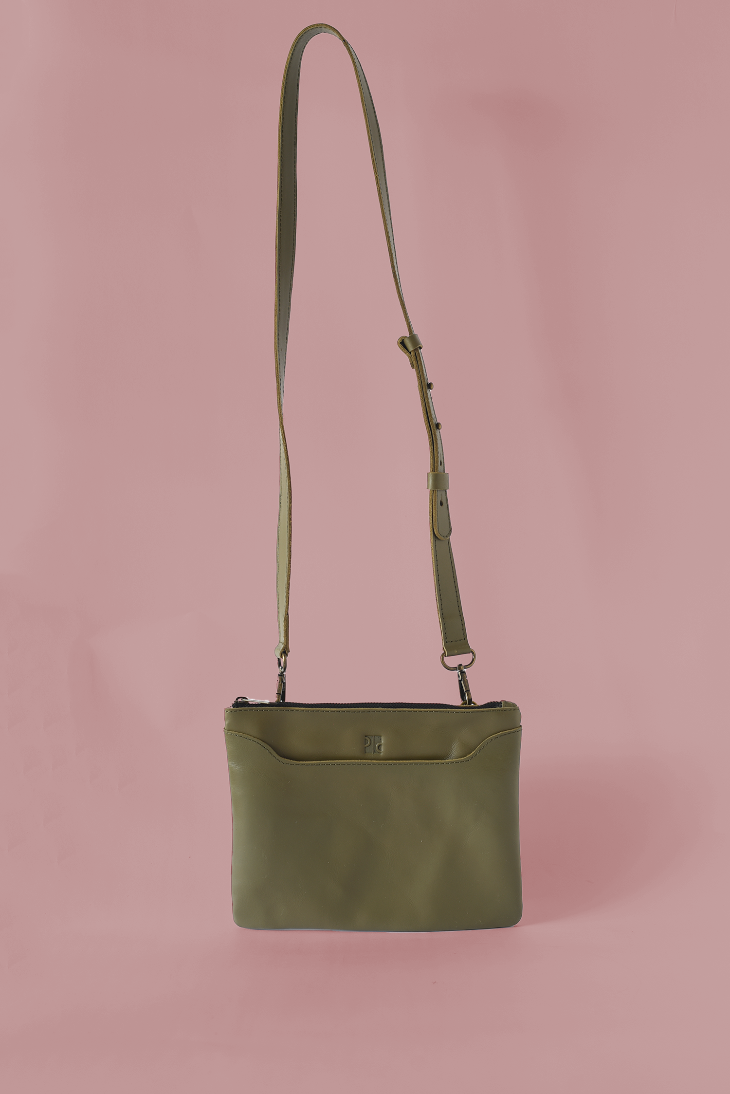 Green leather crossbody bag on a pink background